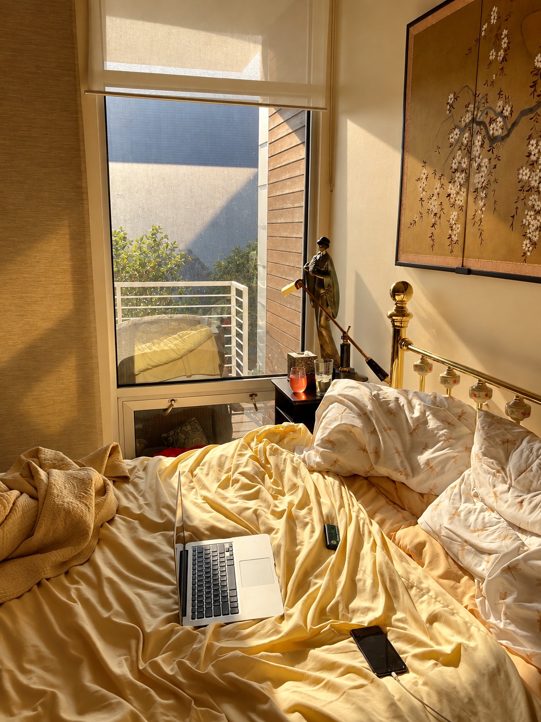 A lived-in bed with a laptop in golden afternoon light