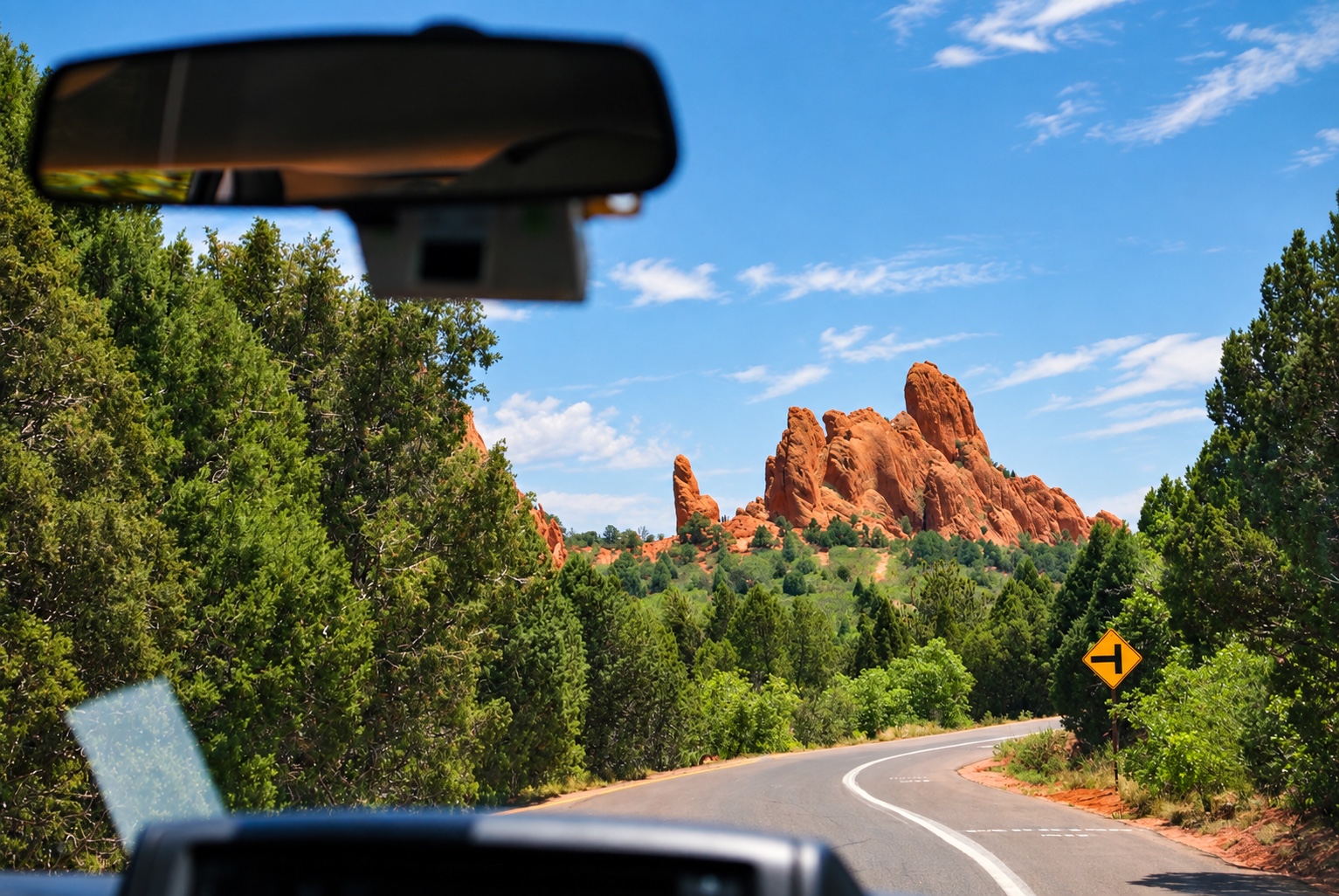 Red rock formations seen through a car windshield on a sunny road trip