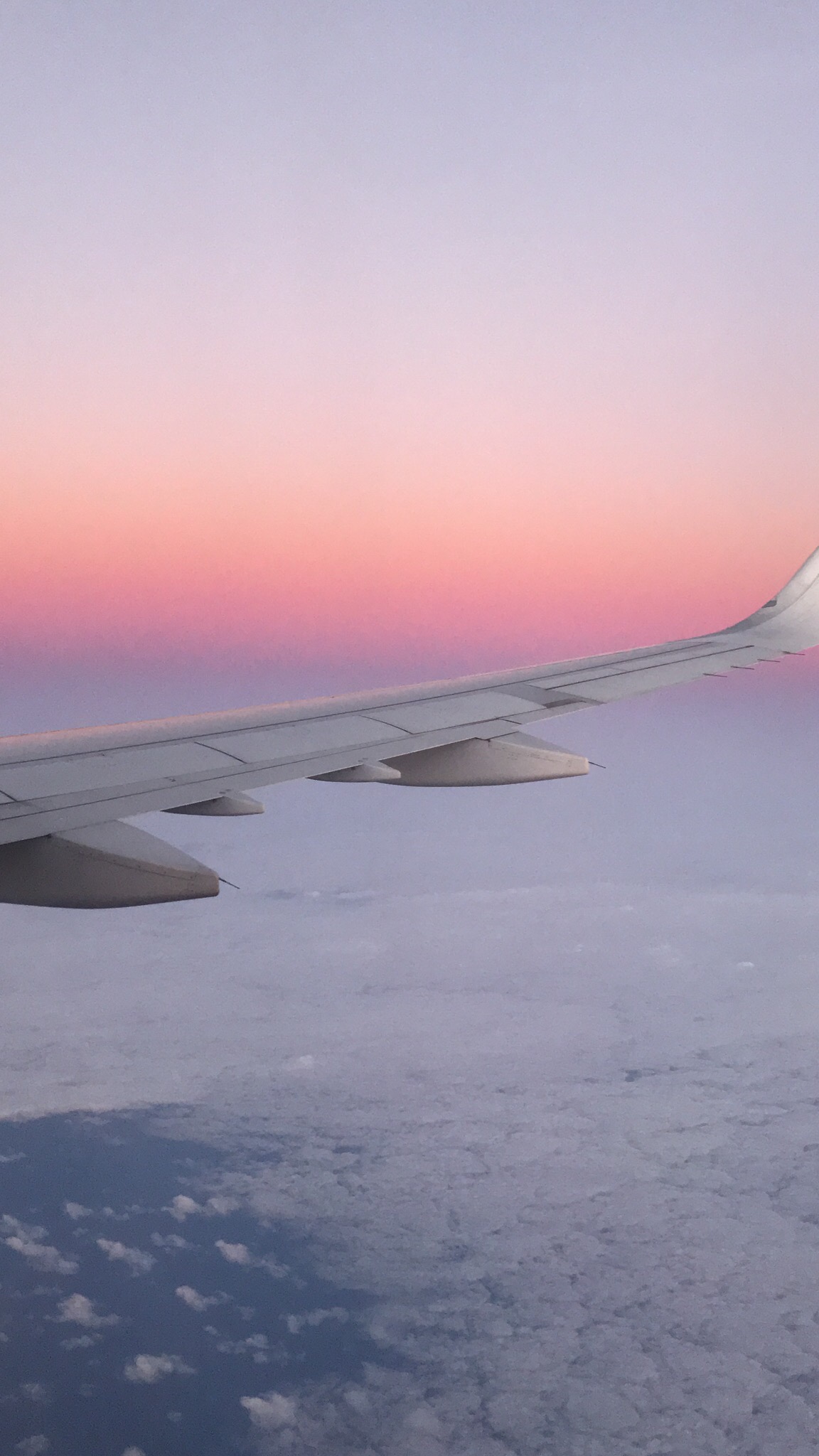 An airplane wing against pink and lavender evening skies