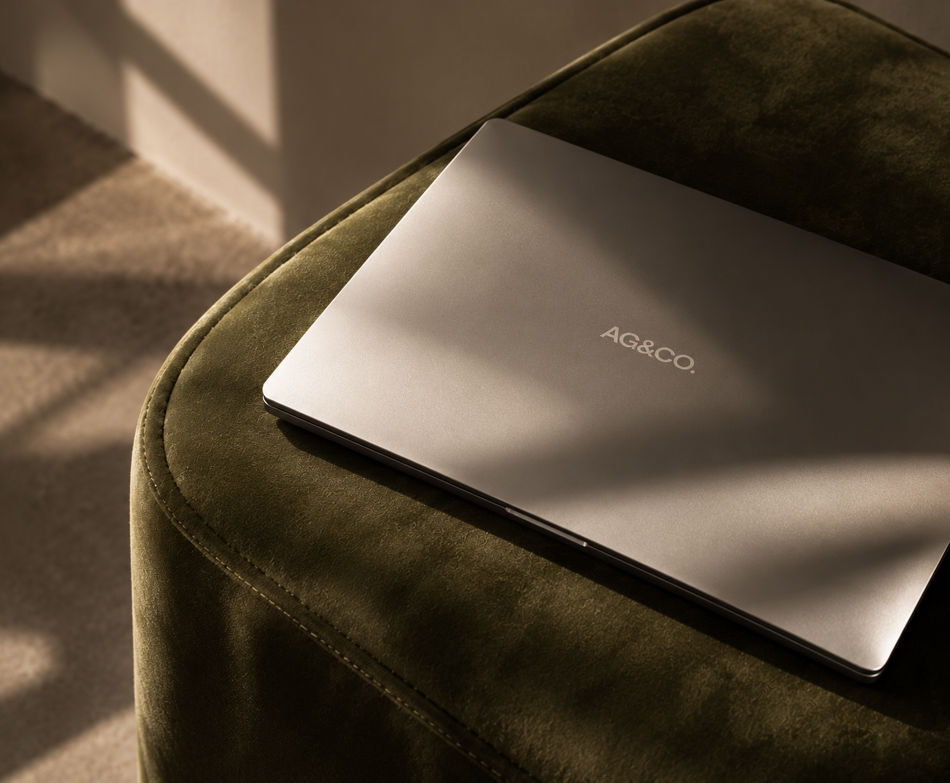 Closed silver AG&CO. laptop on an olive green ottoman